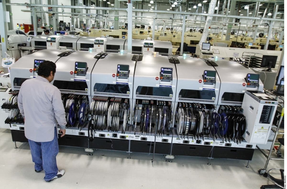 Operario supervisa máquinas de manufactura de componentes electrónicos en planta industrial.