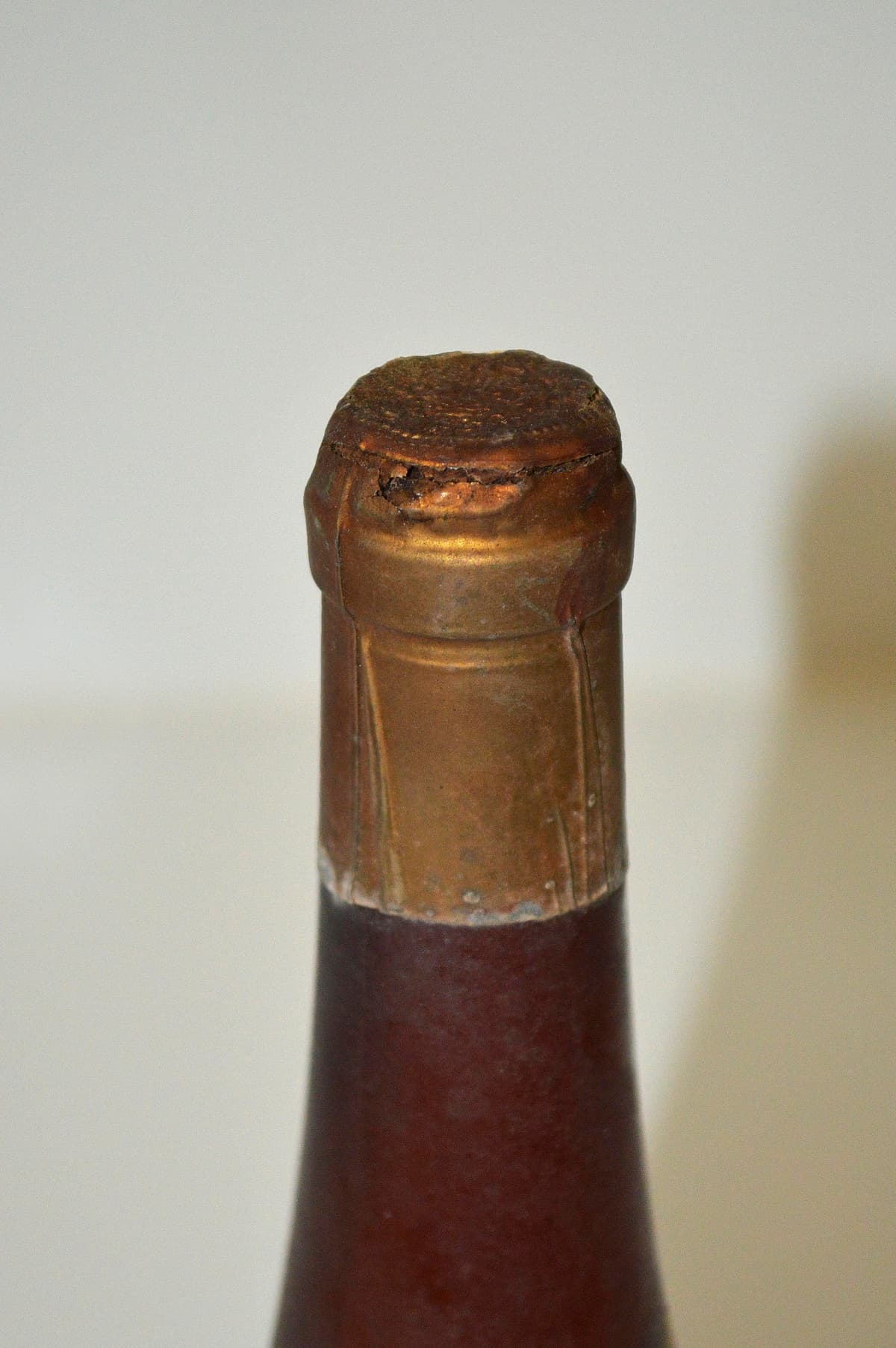 Detalle del cuello y boca de una botella de vidrio oscuro con oxidación en la cápsula metálica superior.