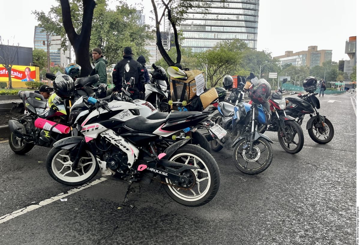 Grupo de trabajadores en motocicletas y motos taxi estacionadas en una avenida urbana durante una concentración o manifestación.